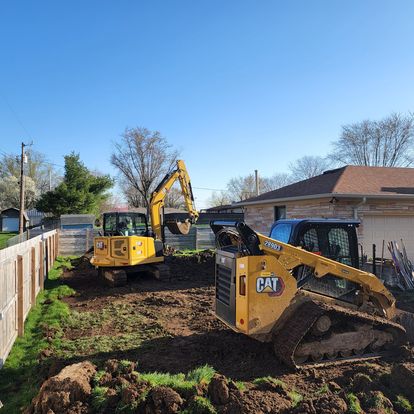 Two construction digging machines sit in a side yard of a residential home. 