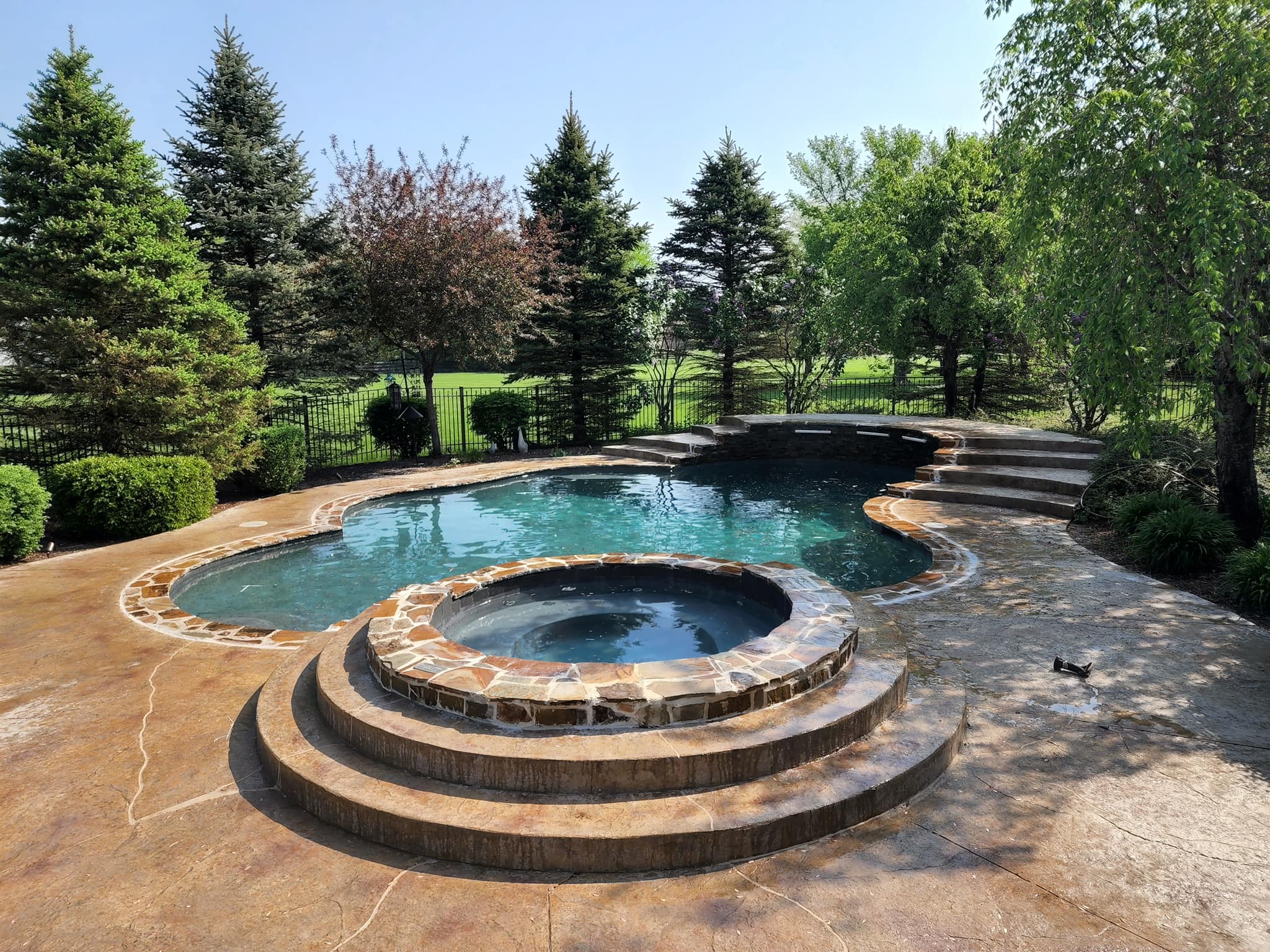 Custom outdoor pool with incorporated custom hot tub. Stamped concrete patio surrounds the pool and hot tub.