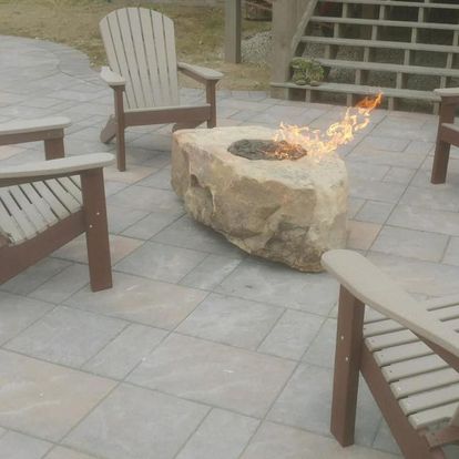 Stone fire pit in the center of four Adirondack chairs on a tiled patio. 